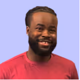 Smiling man with a beard, short hair, and wearing a red shirt against a purple background.