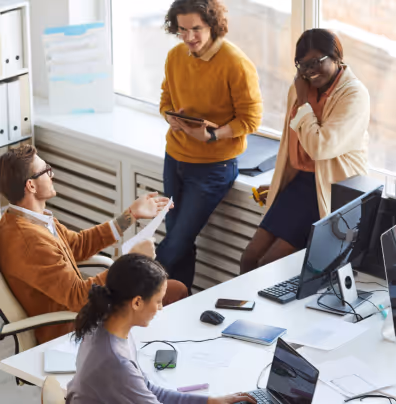 Four colleagues collaborating in a bright office with computers and documents.
