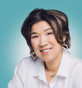 Smiling woman with short black and brown hair wearing a white shirt against a teal background.