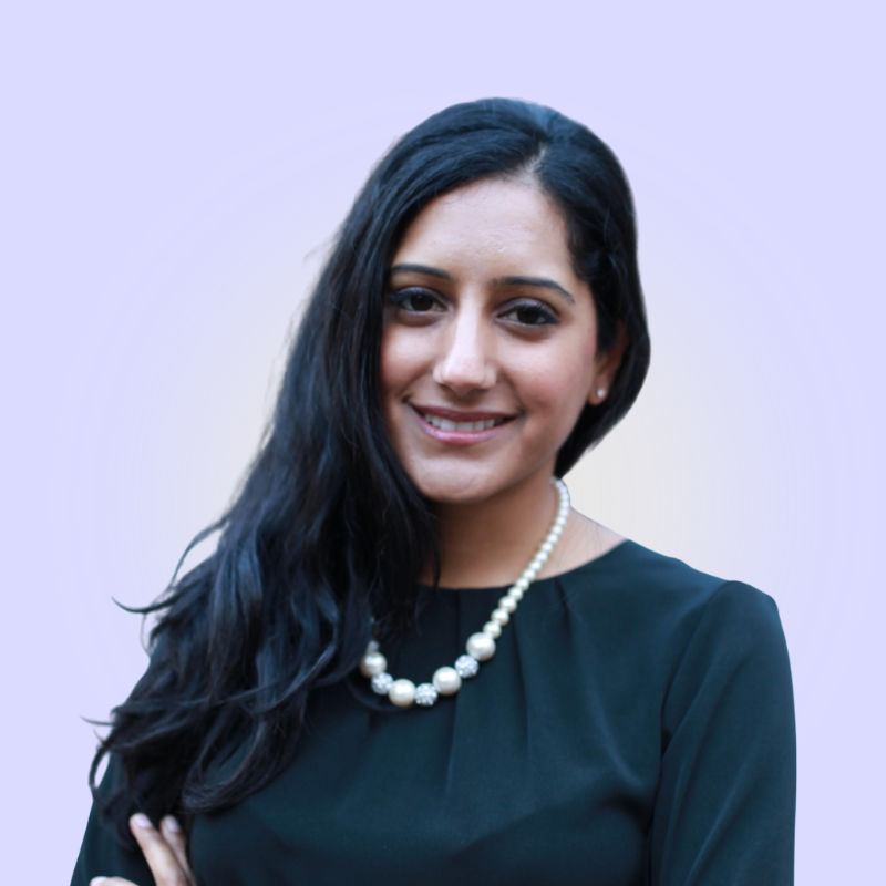 Young woman with long black hair wearing a black top and pearl necklace smiling against a light blue background.