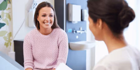 Young woman in a pink sweater smiling while talking to a healthcare professional in a clinic.
