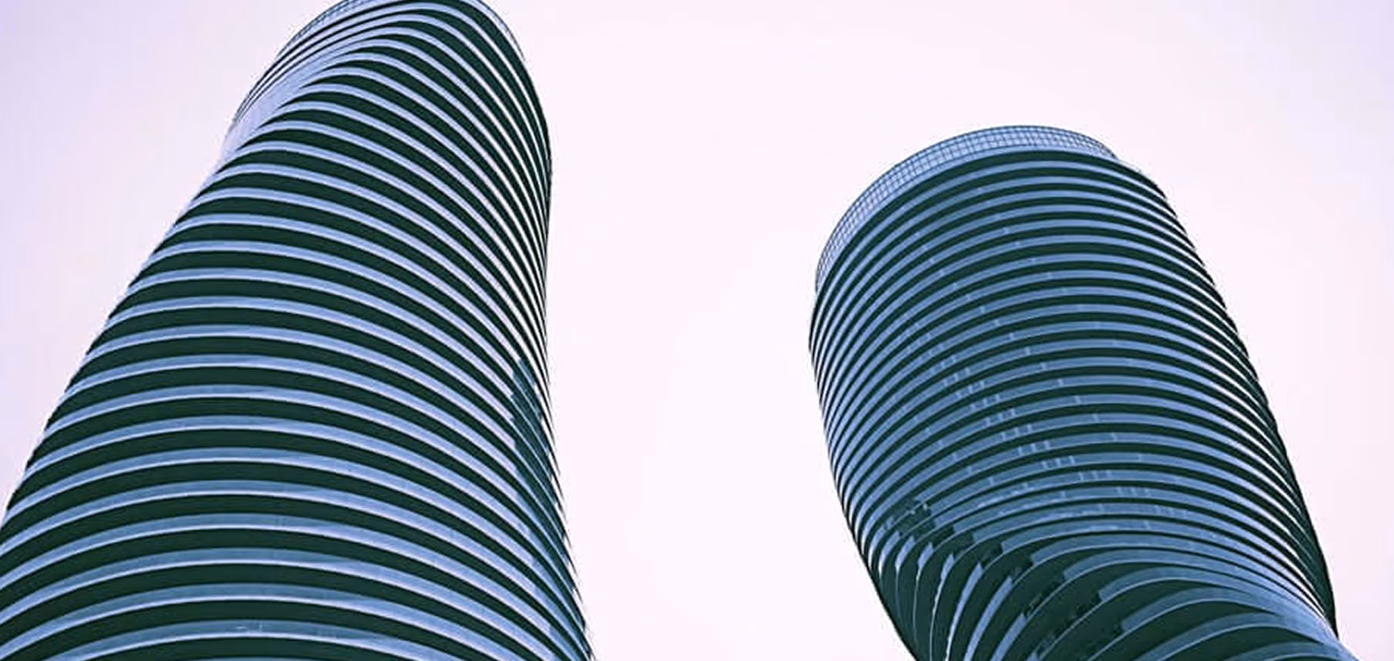 Two modern, curved high-rise buildings with horizontal lines against a pale sky.