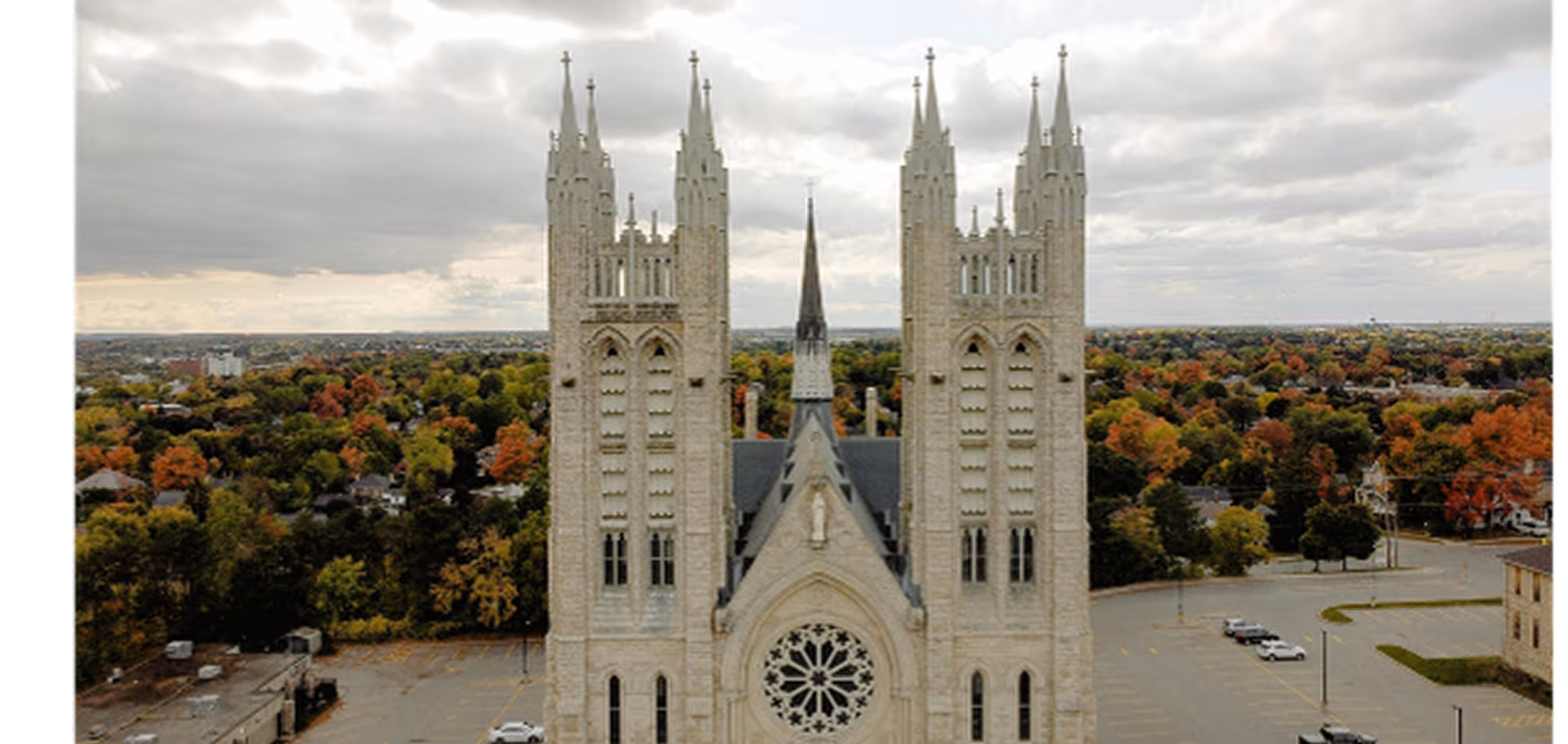 Gothic-style cathedral with two tall spires and a large circular stained-glass window, surrounded by autumn trees.