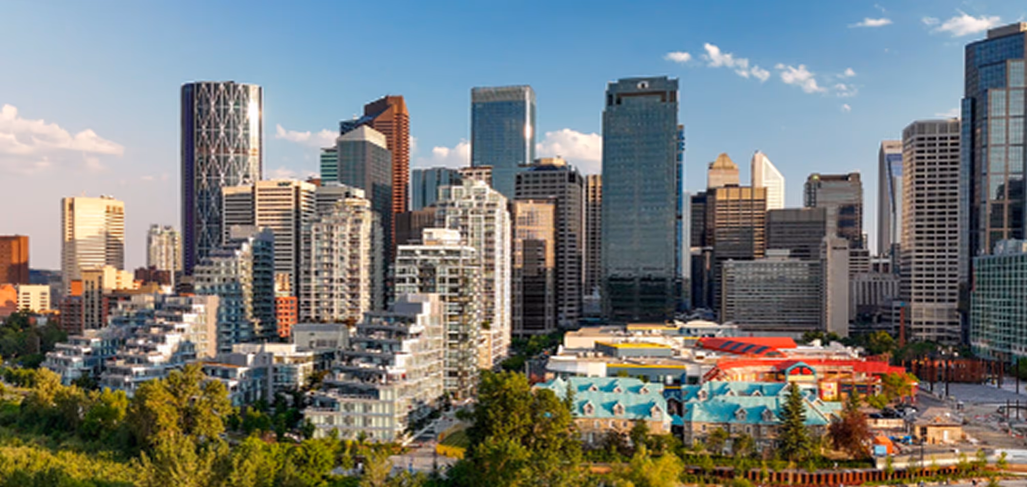 City skyline with modern skyscrapers and green trees under a clear blue sky.