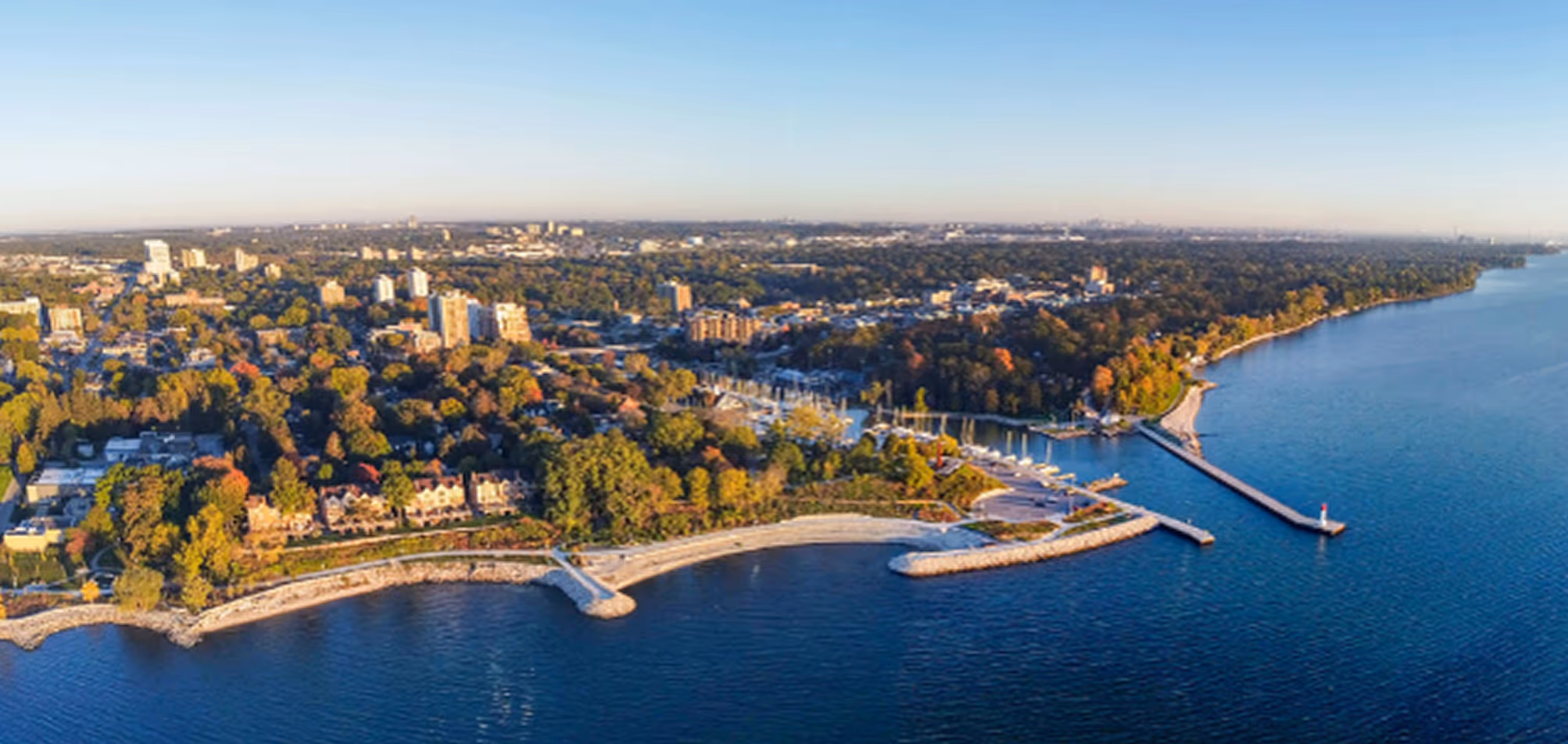 Aerial view of a coastal cityscape with a marina, waterfront park, and residential buildings surrounded by trees.