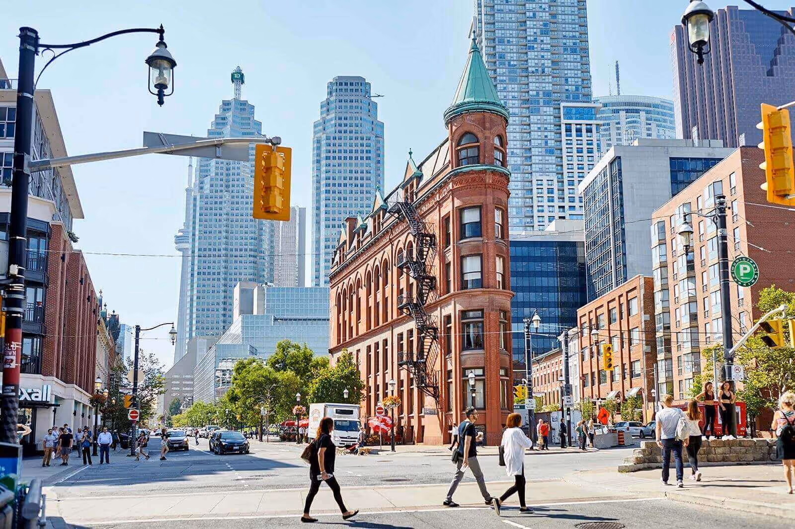 Urban street scene with people crossing and historic red brick building with modern skyscrapers behind.