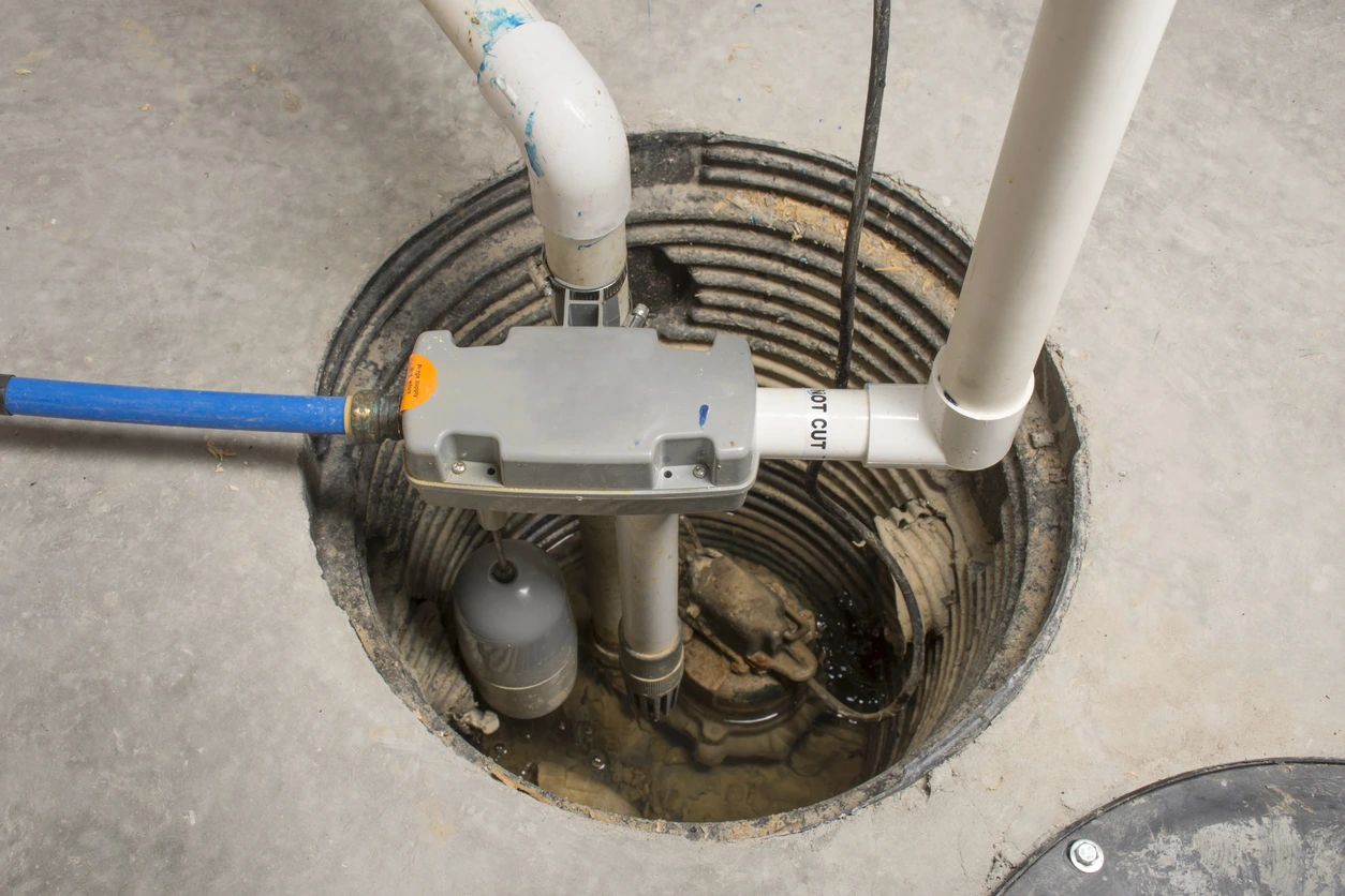Sump pump system installed in a circular pit with pipes and a float switch inside a concrete floor.