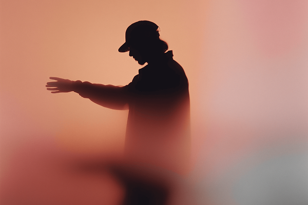 Silhouette of a person wearing a cap with an outstretched arm against a gradient background.