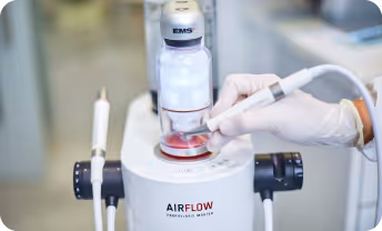 Hand wearing a glove holding a dental tool operating an EMS Airflow Prophylaxis Master device.