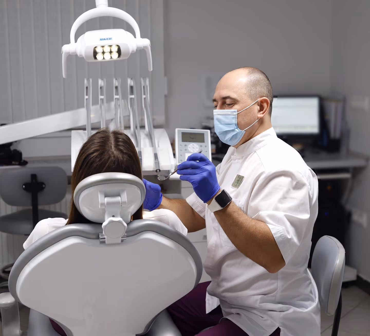 Dentist wearing a mask and gloves examining a patient's teeth in a dental clinic.