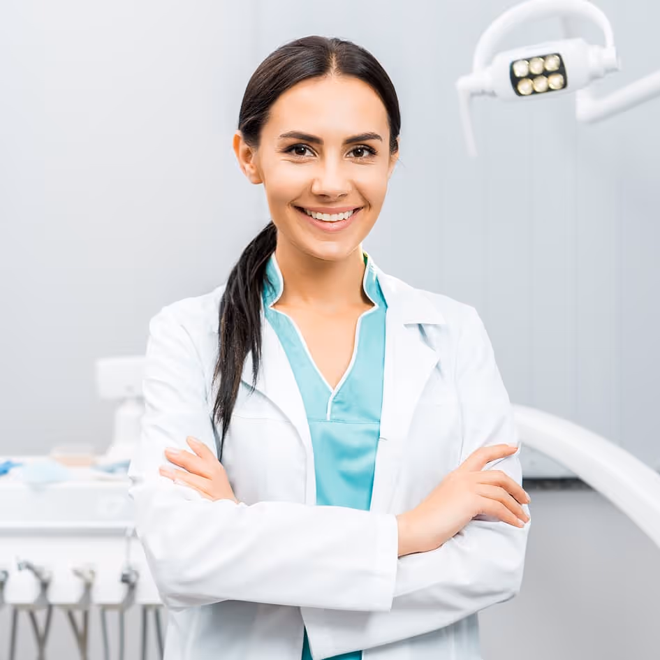 Smiling female dentist in white coat with arms crossed in a dental clinic.