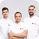 Three men standing side by side against a plain white background, two wearing white shirts and one in a black shirt.
