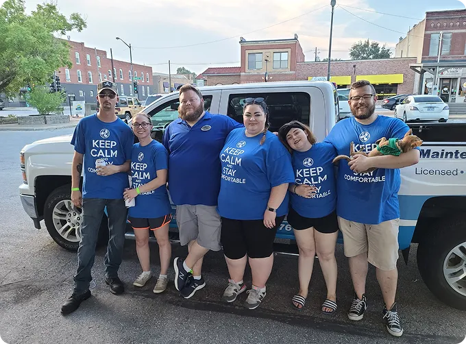 A group of six people in blue shirts promoting HVAC services near a pickup truck.
