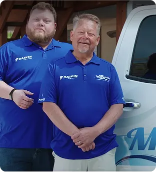 Two professionals in blue Daikin polos stand next to a branded service vehicle, representing air conditioning services.
