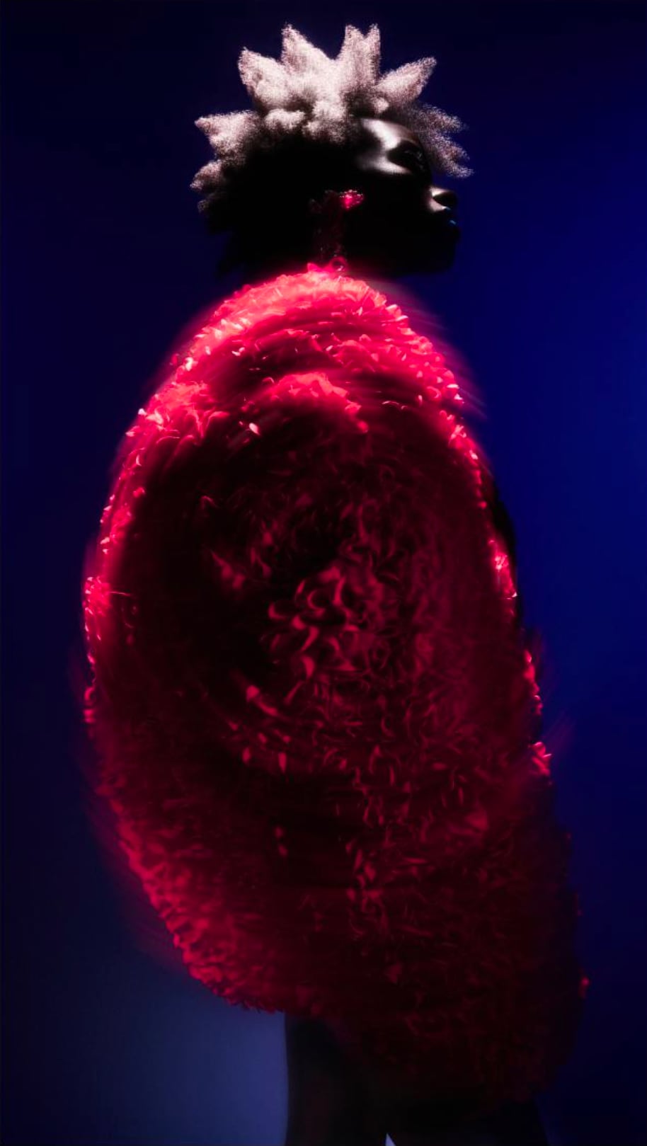 Profile of person with textured, spiky hair wearing a glowing red textured garment against a dark blue background. - from the Magazine NUMÉRO Aurora 12 - Lure of the sea