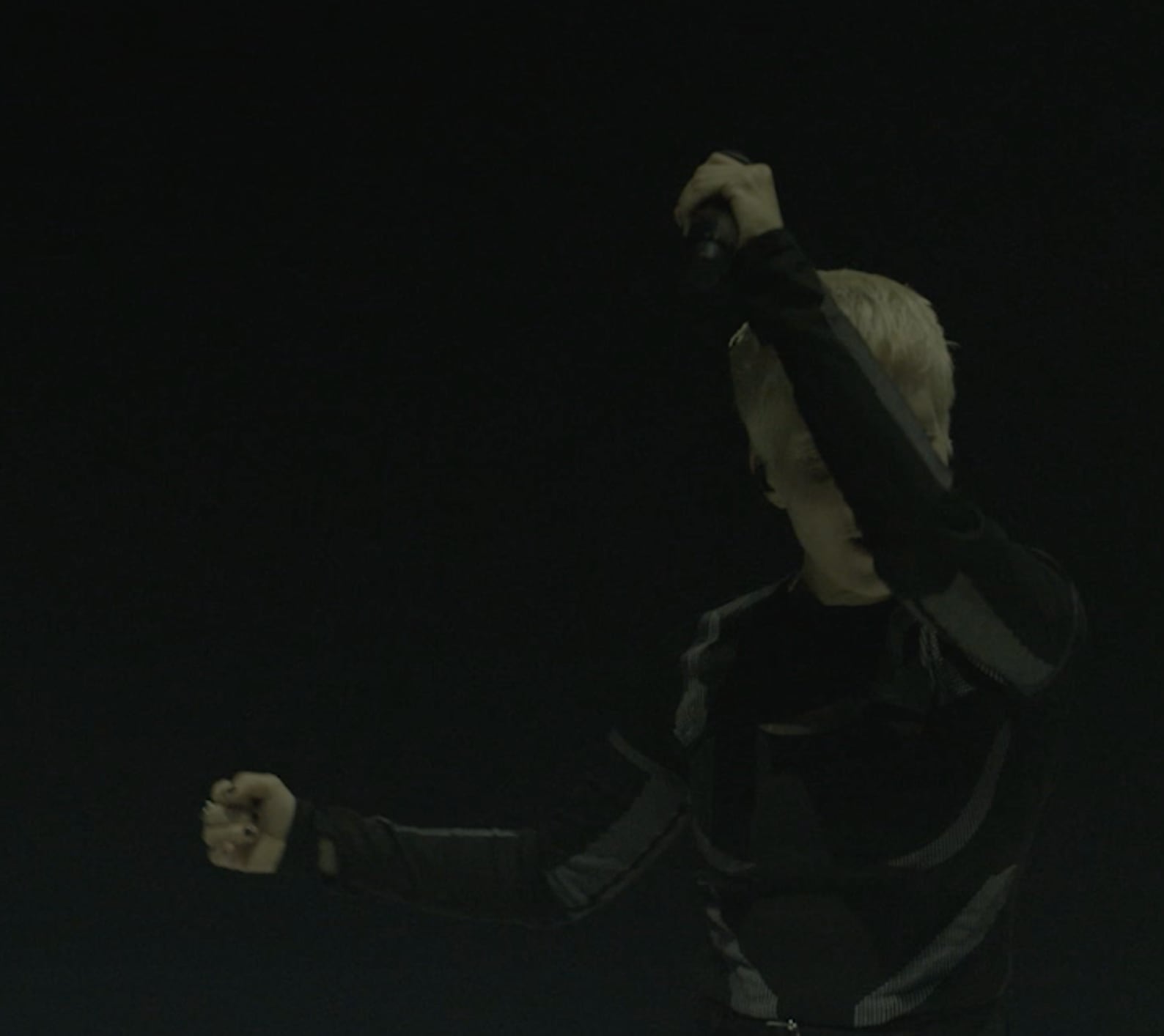 Jeanne Added with short blonde hair wearing dark clothing holding a microphone up with one hand in a dark setting. - screenshot of the videoclip JEANNE ADDED, Both Sides