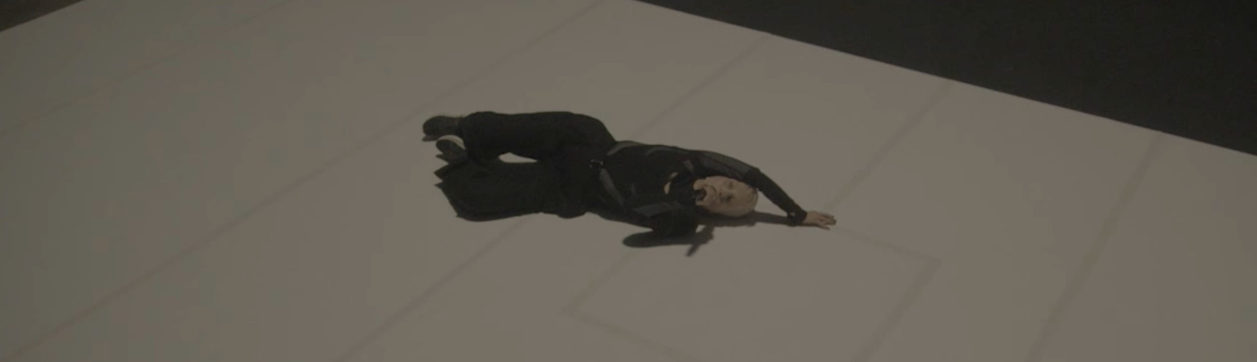 Jeanne Added dressed in black lying on their side on a large light-colored floor with a dark background. - screenshot of the videoclip JEANNE ADDED, Both Sides