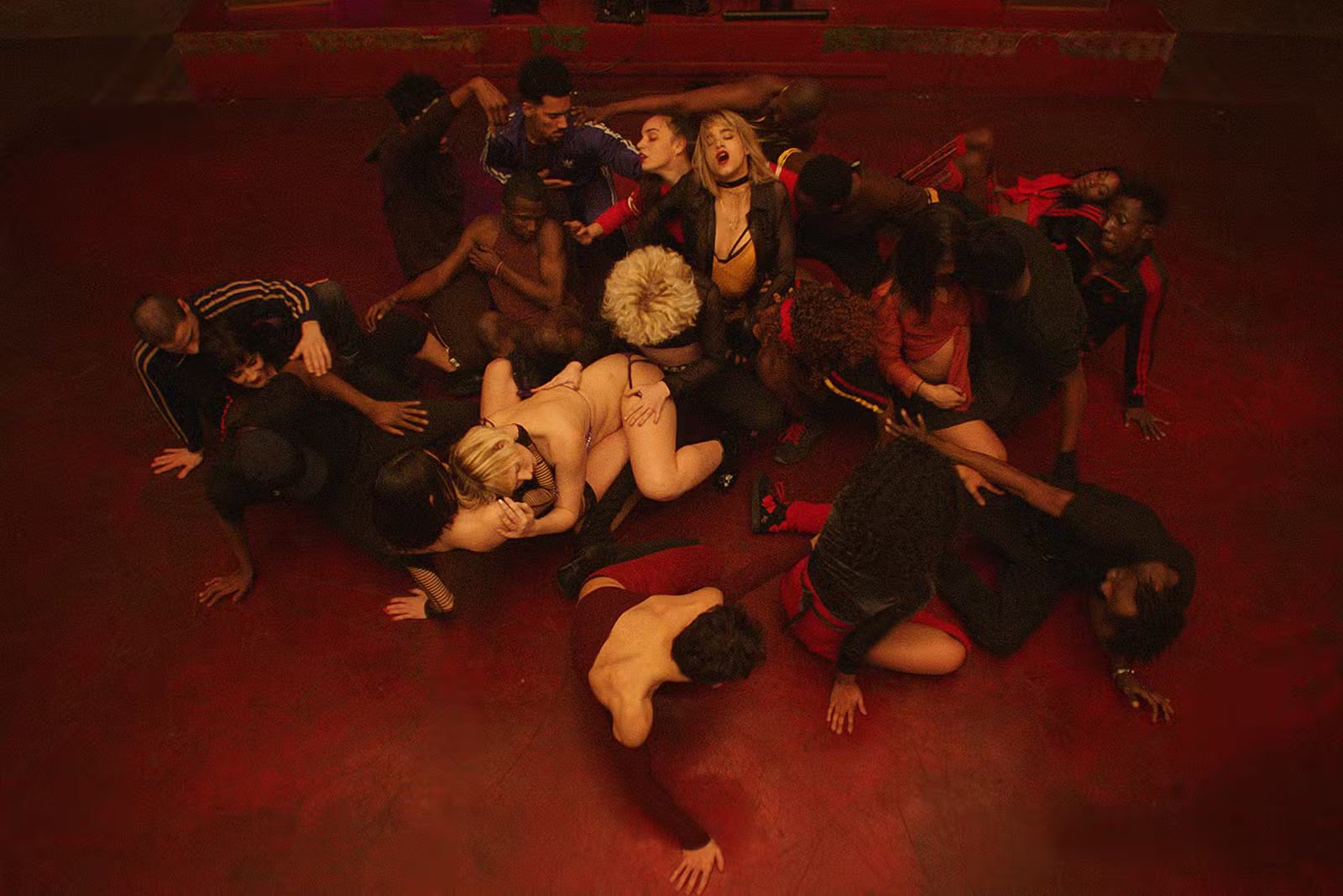 Group of people closely intertwined on a red floor, engaging in an expressive, intimate dance or performance. - screenshot of the film CLIMAX