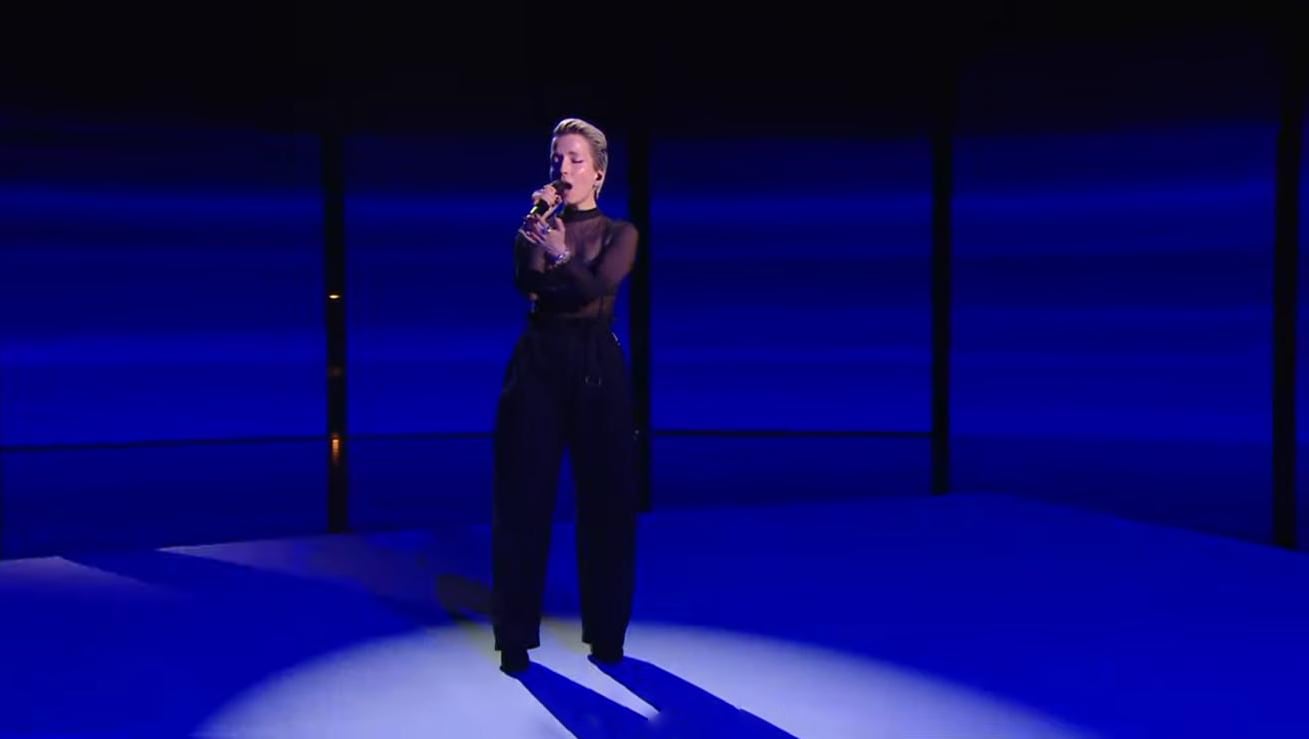 Jeanne Added wearing black sheer top and pants singing into a microphone on a blue-lit stage with a spotlight. - screenshot of the live performance of JEANNE ADDED x La Créole - Mutate during Les Victoires de la Musique