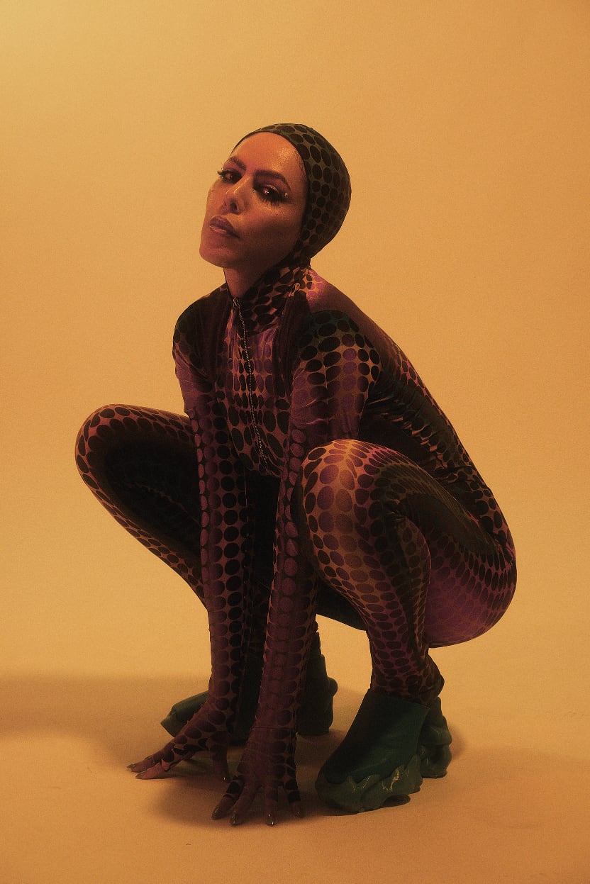 SABRINA BELLAOUEL wearing a purple and black polka dot bodysuit and matching head covering against a warm beige background.