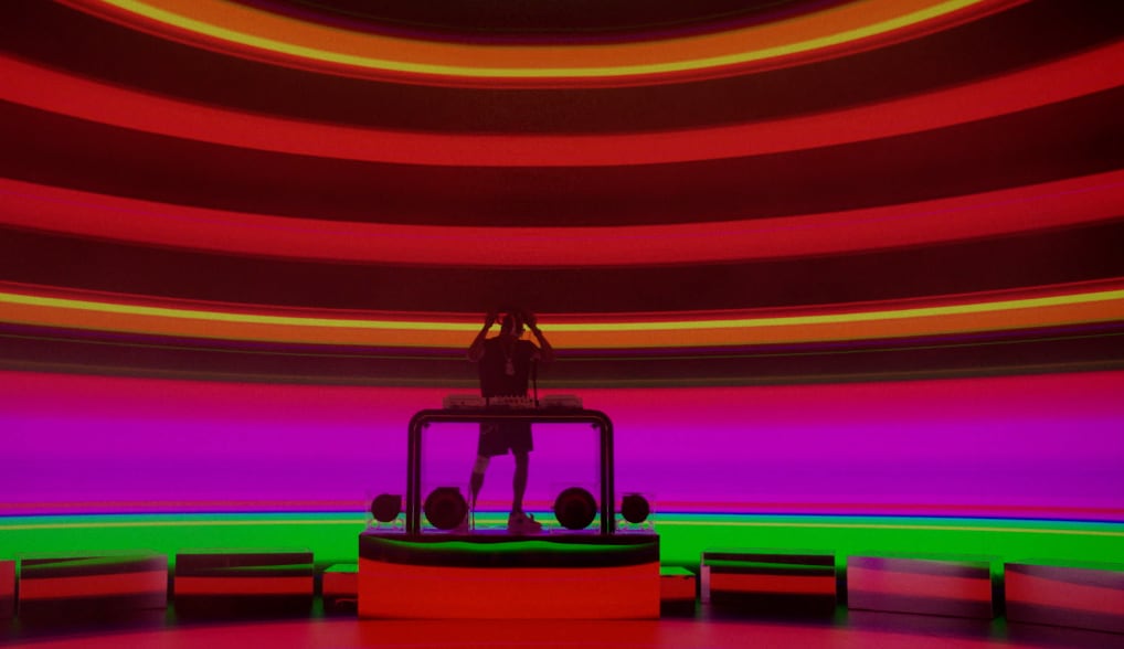 Silhouetted DJ performing on a circular stage with vibrant horizontal neon stripes in red, purple, and green wrapping around a dome-shaped room. - Screenshot of the videoclip TRAVIS SCOTT, Modern Jam