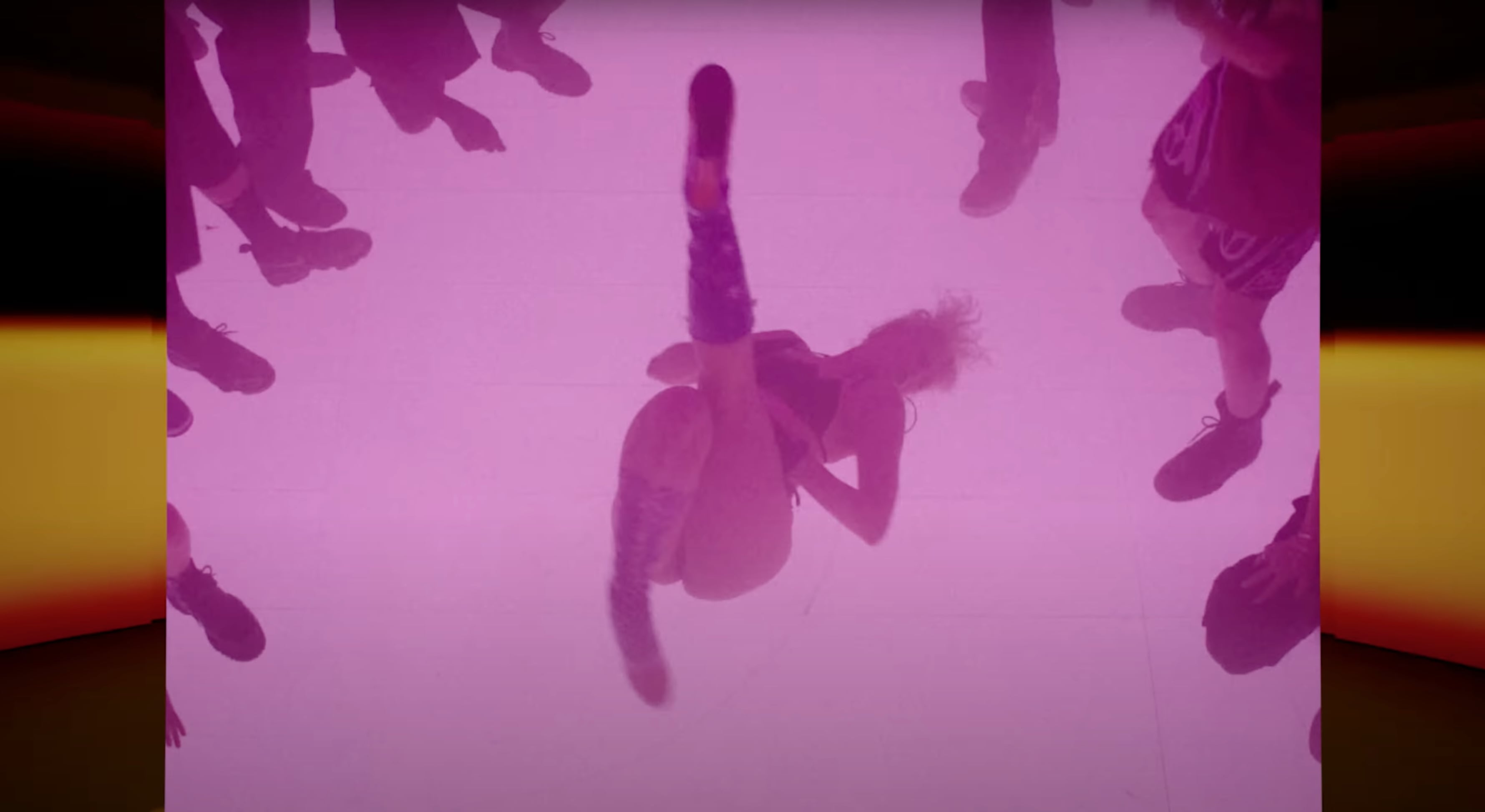 Person breakdancing on a floor lit with pink lighting, surrounded by people standing and watching. - Screenshot of the videoclip TRAVIS SCOTT, Modern Jam