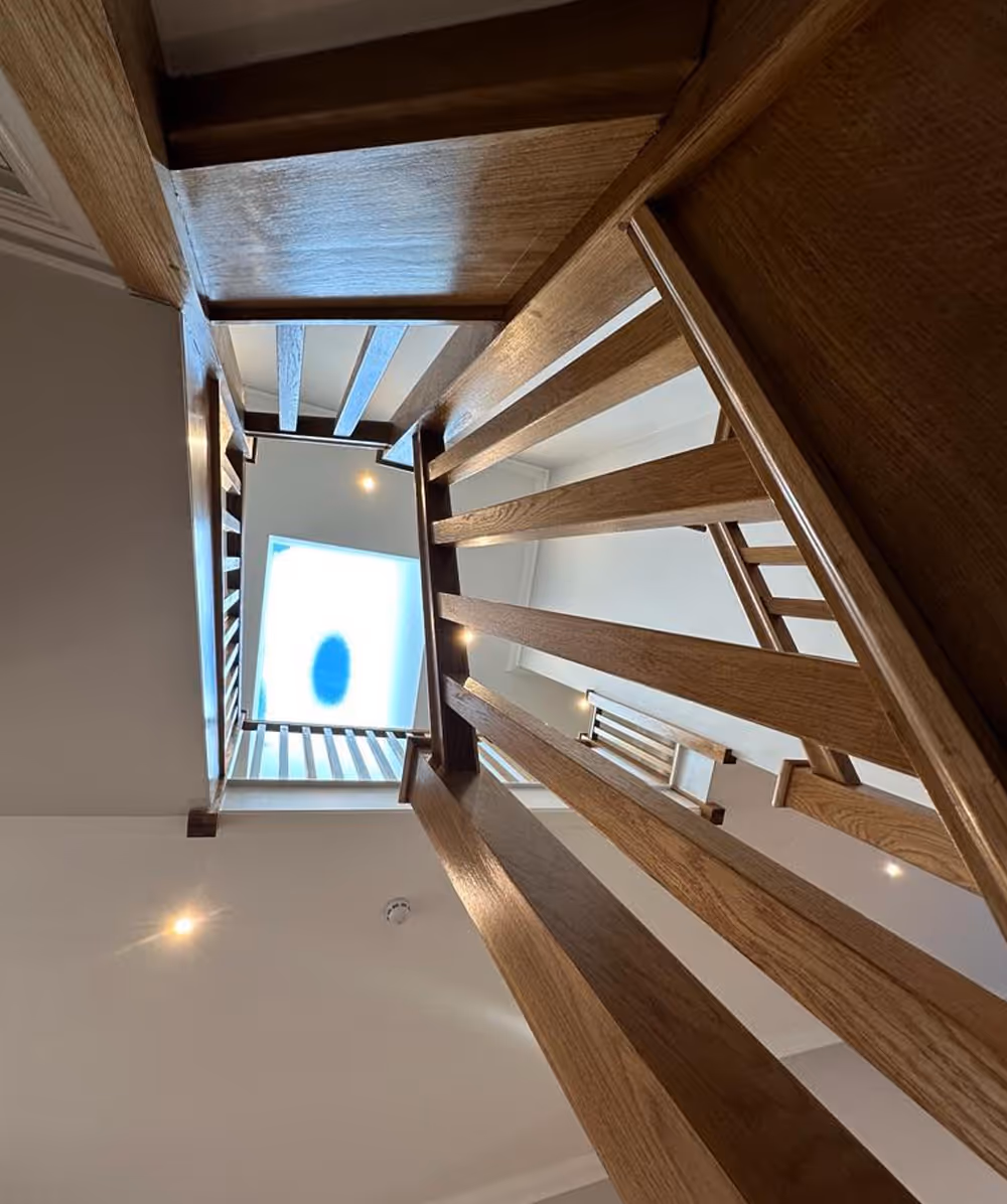 Upward view of a wooden staircase with natural light coming through a ceiling window. Province Group Construction.
