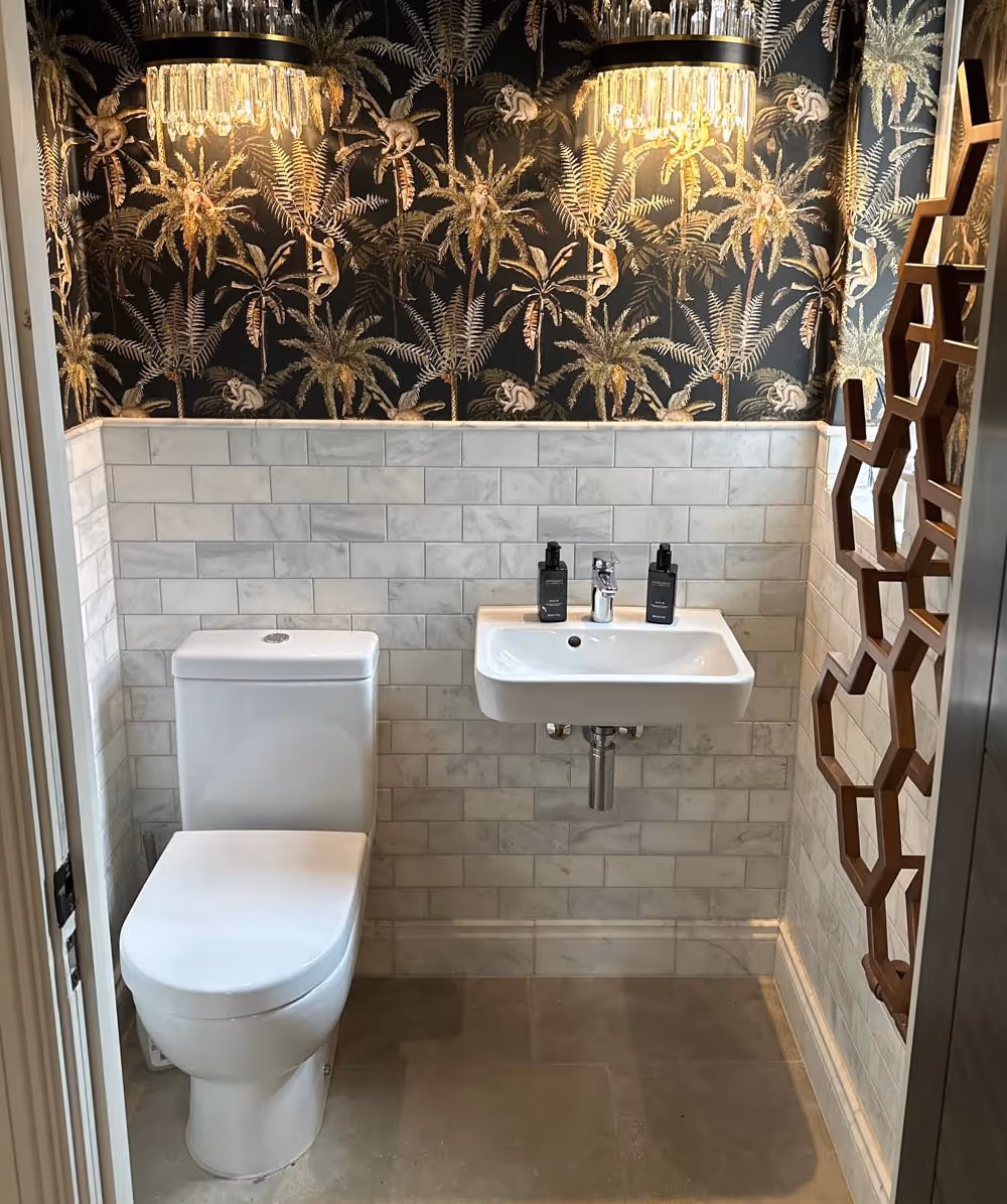 Small bathroom with a white toilet and wall-mounted sink, decorated with monkey and palm tree wallpaper and crystal light fixtures. Province Group Construction.