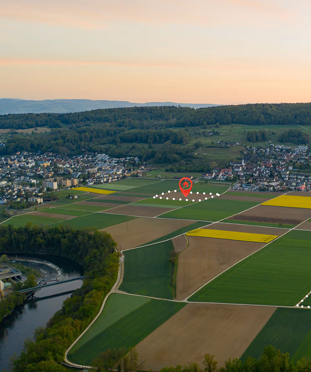 Aerial view of farmland plots with a red location marker highlighting a specific parcel near a river and a village at sunset. Province Group Construction.