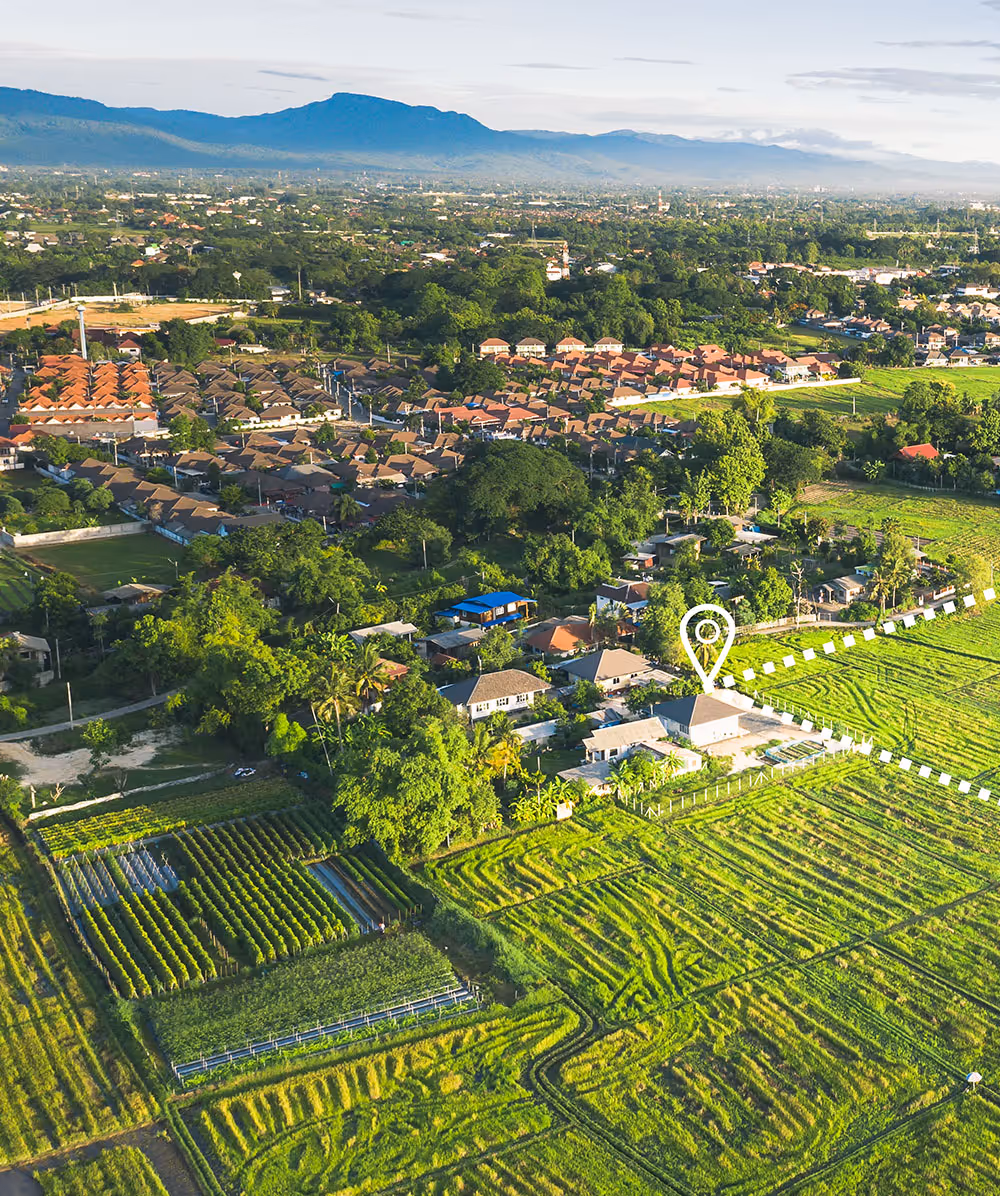 Aerial view of rural landscape with green farmland, houses, and a marked location pinpoint in a small residential area. Province Group Construction.