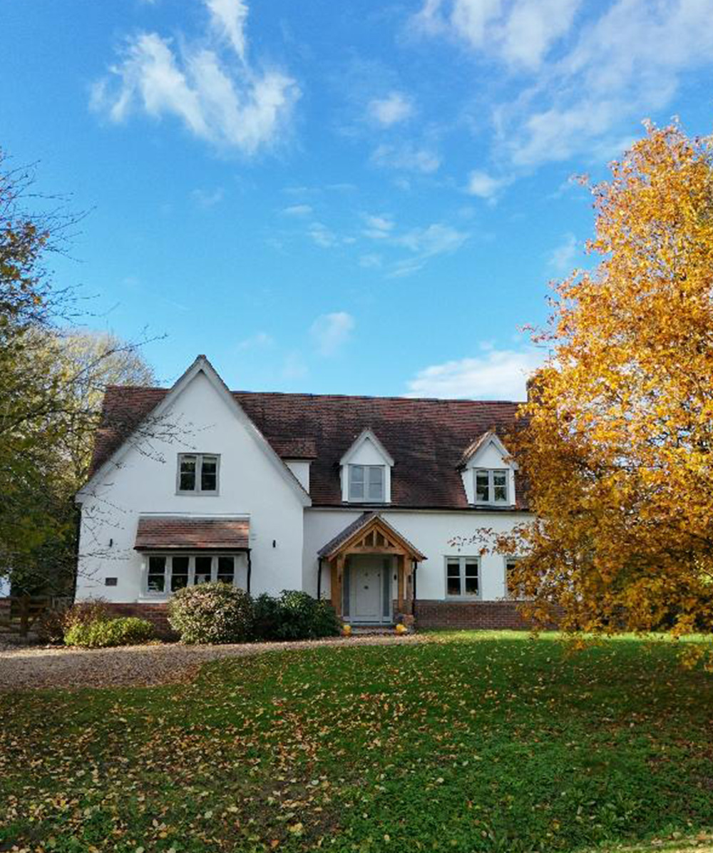 White two-story house with a brown tiled roof, surrounded by green grass and trees with autumn foliage. Province Group Construction.