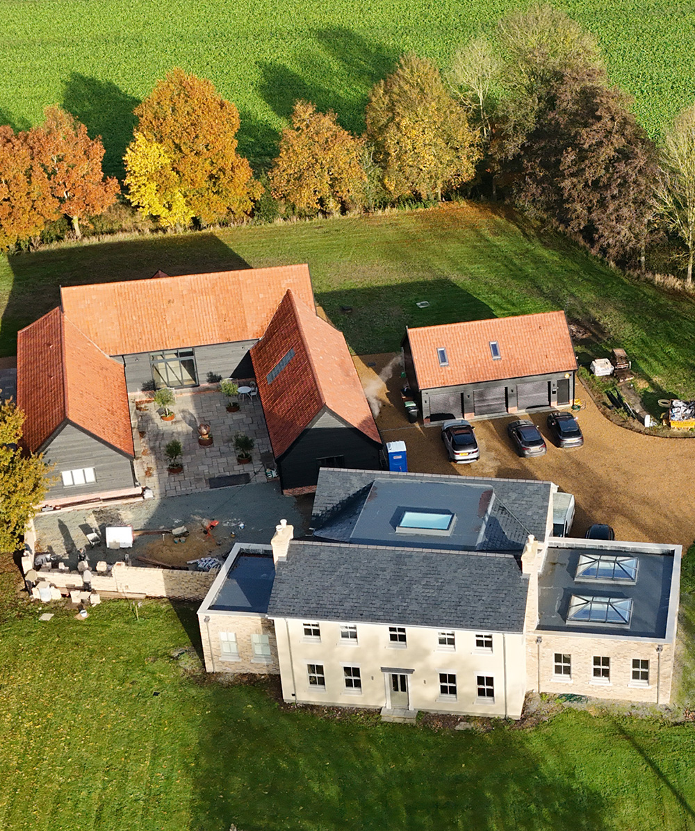 Aerial view of a rural property with multiple buildings including a large cream house and several black-clad structures with orange roofs, surrounded by green grass and autumn trees. Province Group Construction.