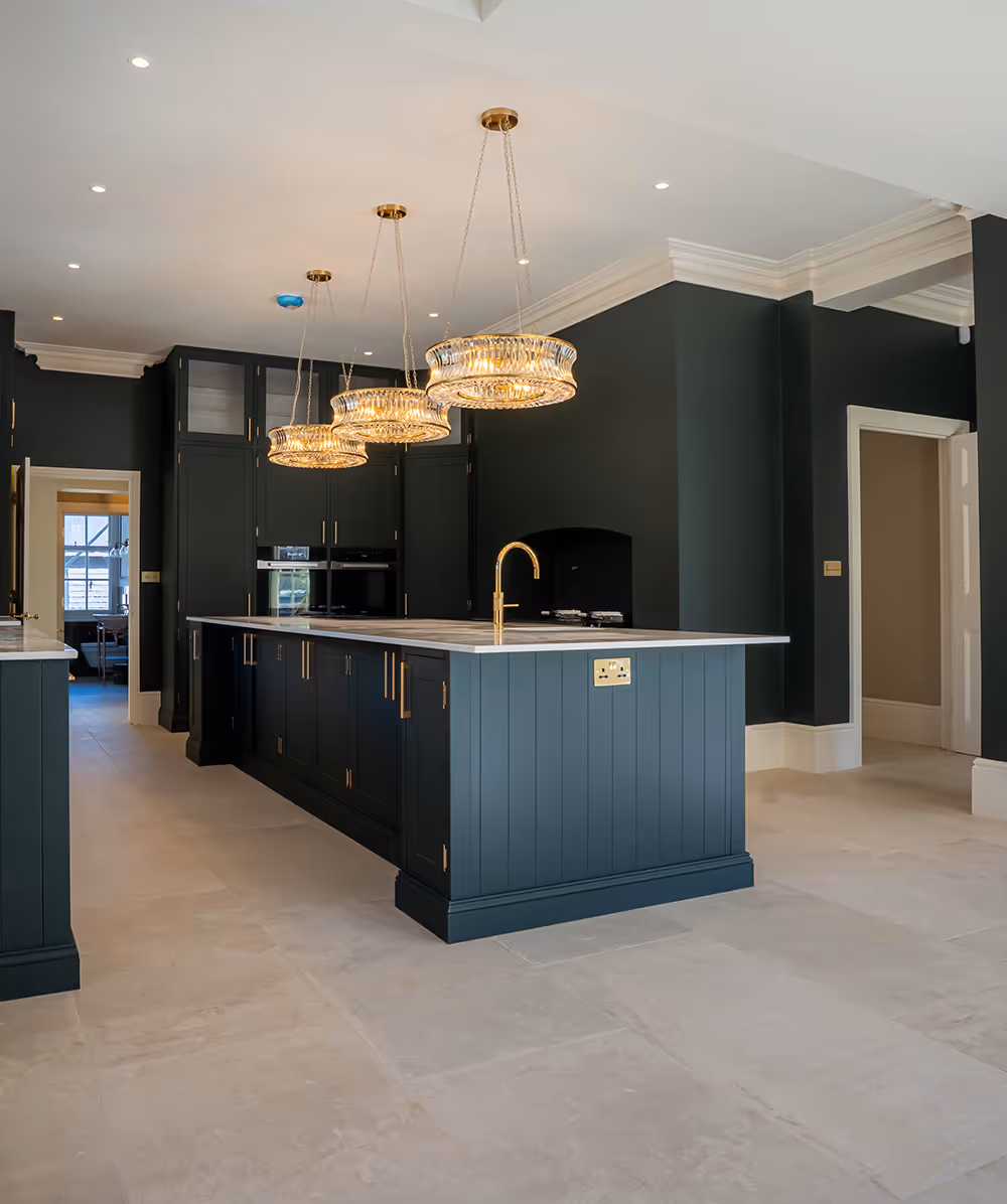 Modern kitchen with dark teal cabinetry, marble countertop island, gold fixtures, and three crystal pendant lights. Province Group Construction.