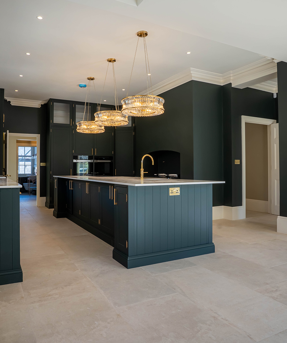 Modern kitchen with dark teal cabinetry, marble countertop island, gold fixtures, and three crystal pendant lights. Province Group Construction.