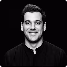 Smiling man with short hair in a black shirt against a black background.