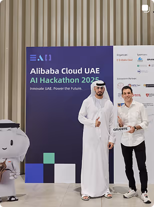 Two men posing with thumbs up at Alibaba Cloud UAE AI Hackathon 2023 event backdrop.
