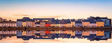 Colorful houses reflected in calm river water under a clear sky at sunrise or sunset.