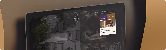 Tablet screen showing Abbey Hotel website with a booking section on a brown background.