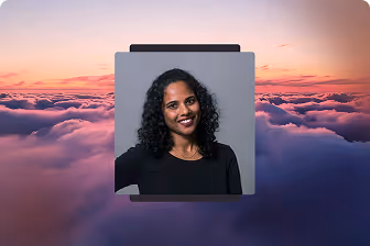 Smiling woman with curly black hair in a black top against a gray background, over a sunset sky with clouds.