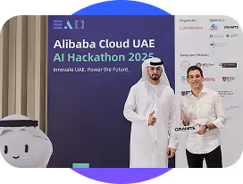 Two men standing in front of Alibaba Cloud UAE AI Hackathon 2025 banner, one in traditional dress.
