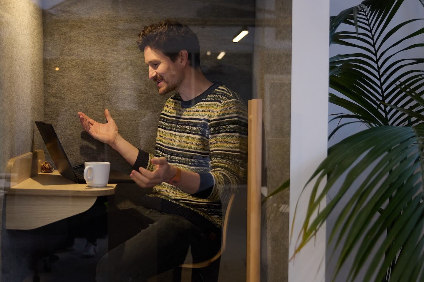 Homme souriant discutant devant un ordinateur portable dans une cabine de travail privée.