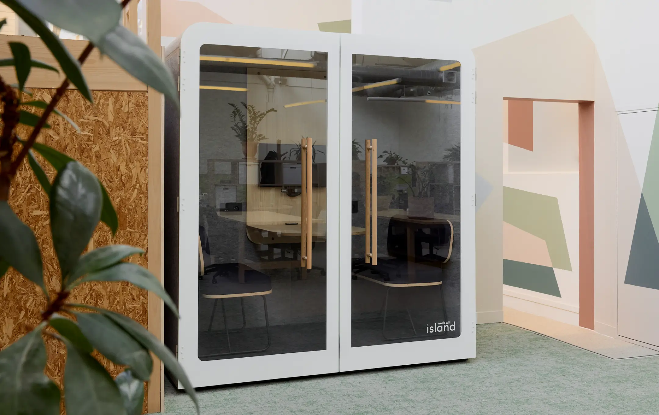 Cabine de bureau insonorisée avec portes vitrées et poignées en bois, deux chaises noires à l'intérieur.