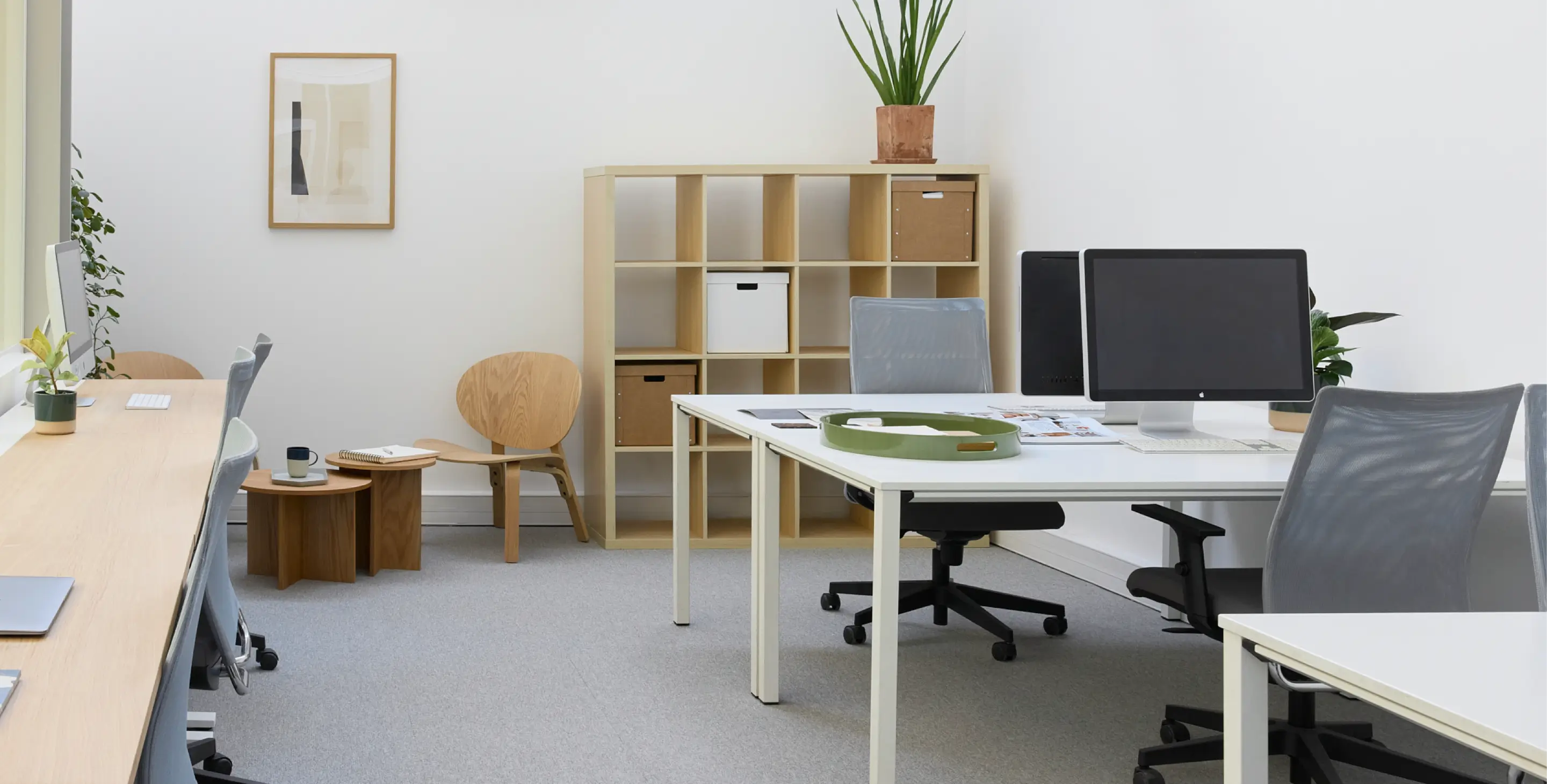 Bureau moderne avec des chaises de bureau grises, ordinateur desktop, étagère en bois avec boîtes de rangement, et plantes d'intérieur décoratives.