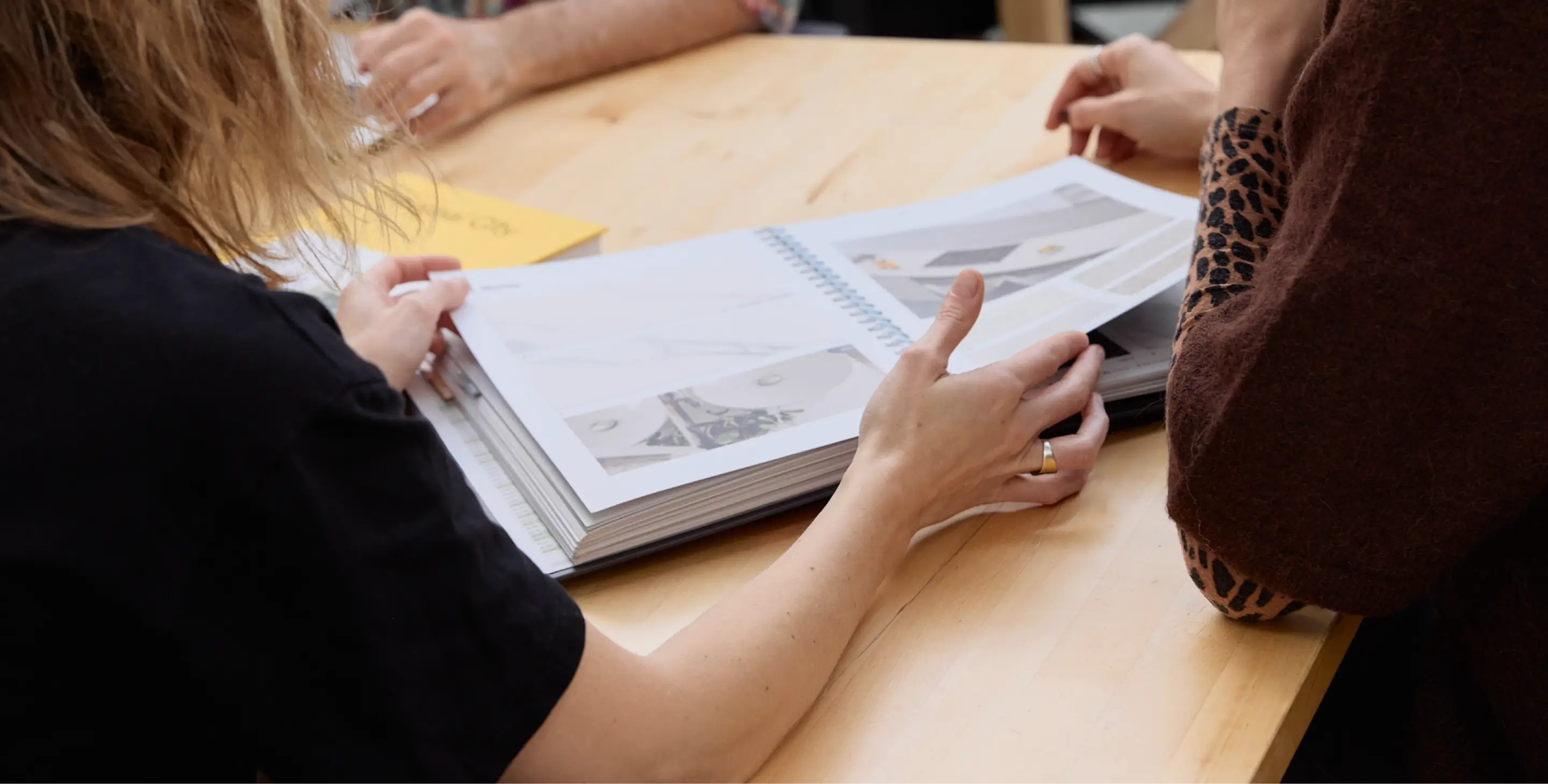 Deux personnes assises à une table en bois regardant un classeur ouvert avec des documents imprimés.