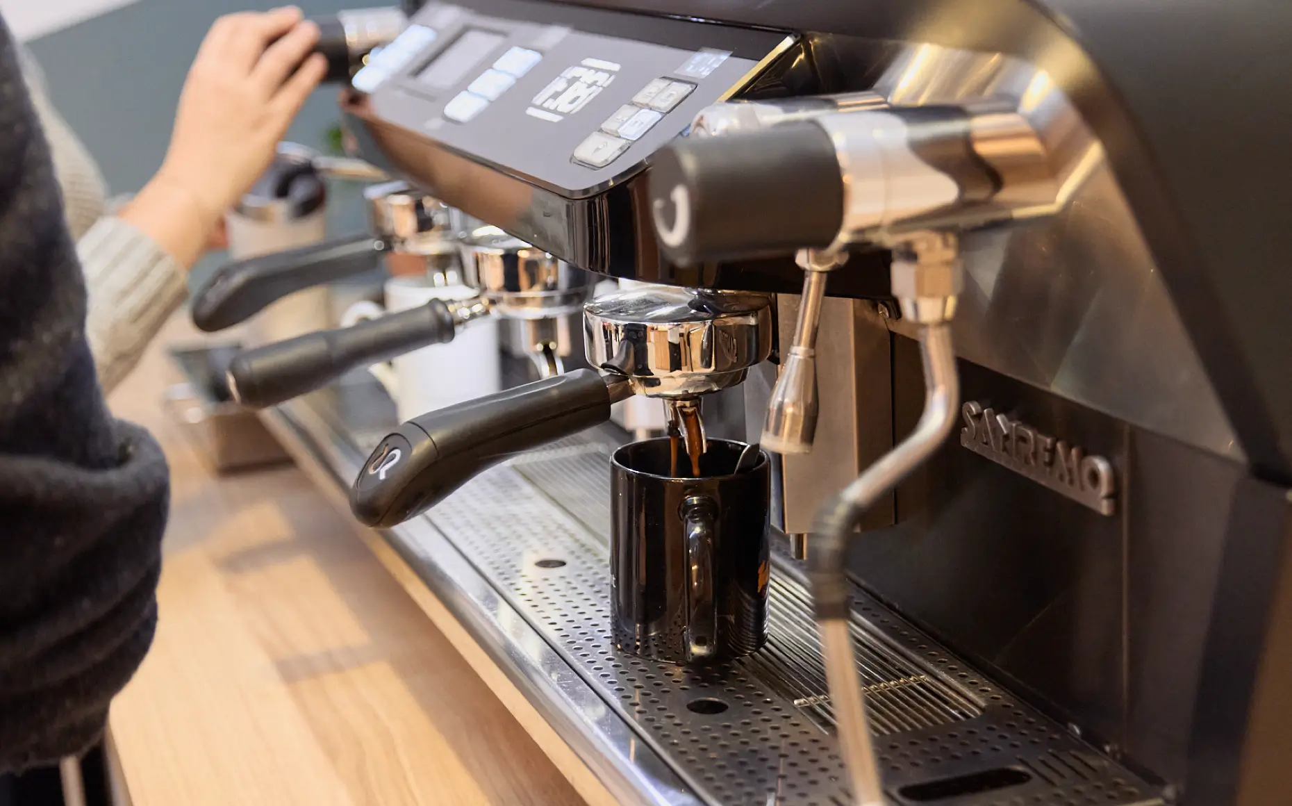 Café coulant d'une machine à espresso professionnelle dans une tasse noire sur un comptoir en bois.