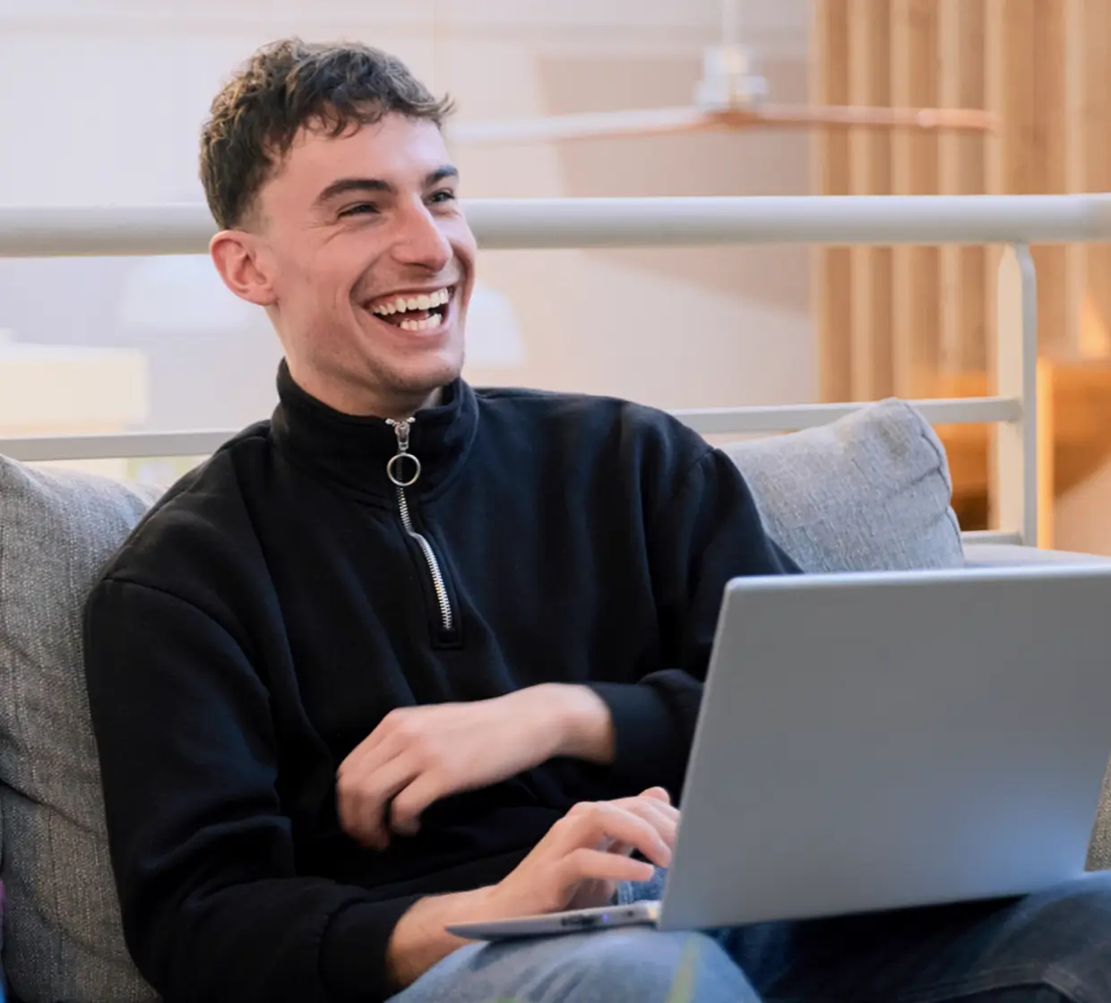 Jeune homme souriant utilisant un ordinateur portable assis sur un canapé.