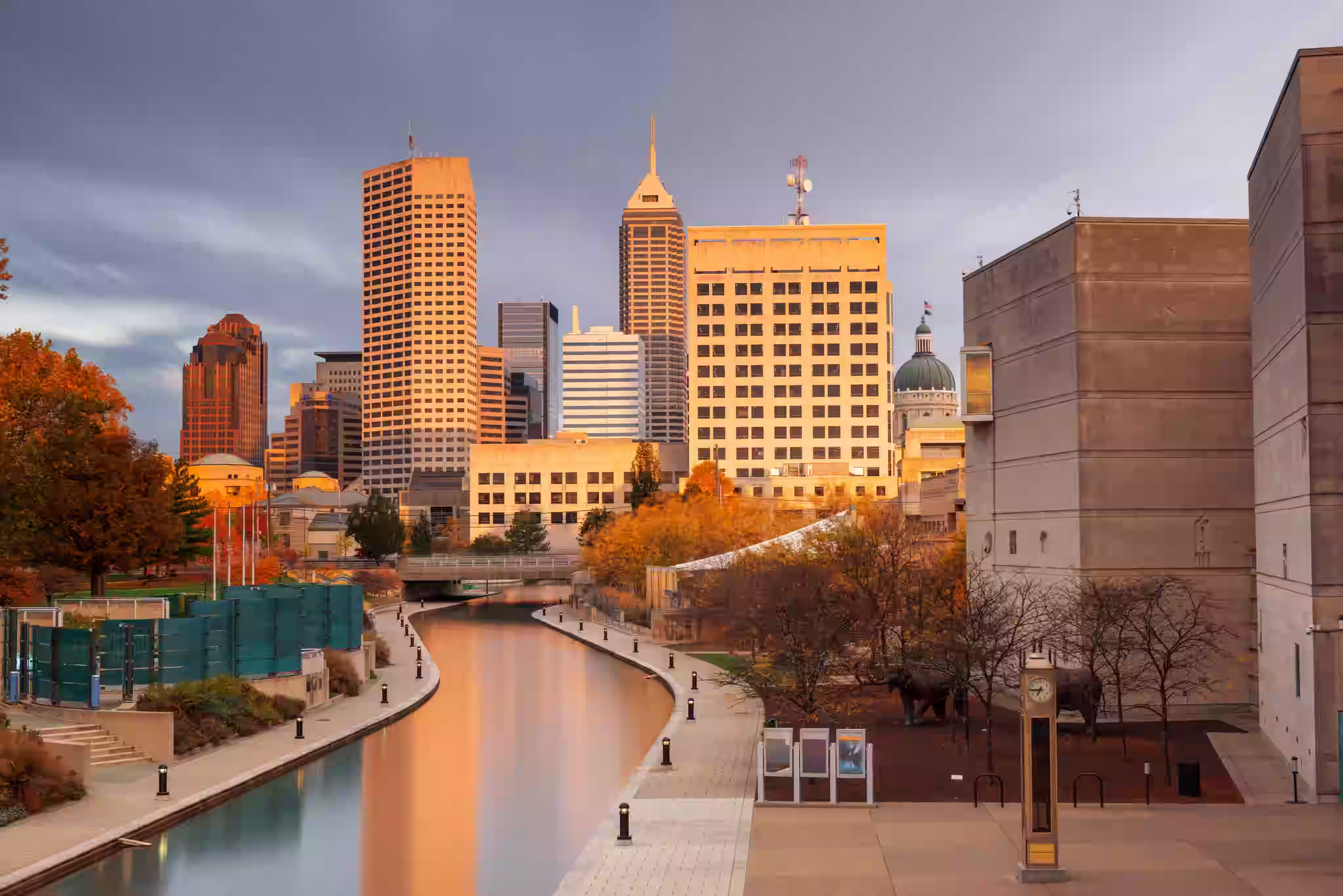 Downtown Indianapolis skyline at sunset with canal and autumn trees along the waterwalk.