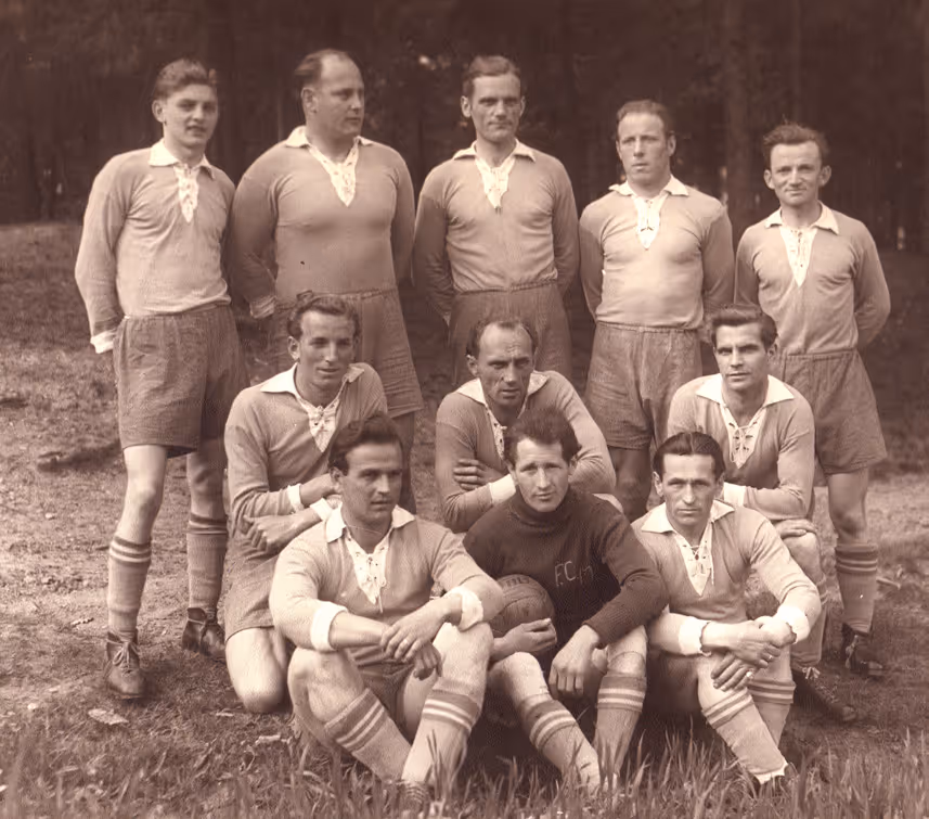 Vintage-Sepiafoto einer zehnköpfigen Fußballmannschaft, die im Freien in langärmeligen Trikots mit Schnürung und Shorts posiert.