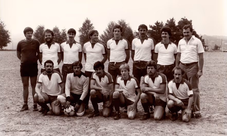 Vintage-Schwarzweißfoto einer Fußballmannschaft mit 15 Männern, die im Freien auf einem Feld posieren, zwei Reihen, einige kniend, andere stehend.