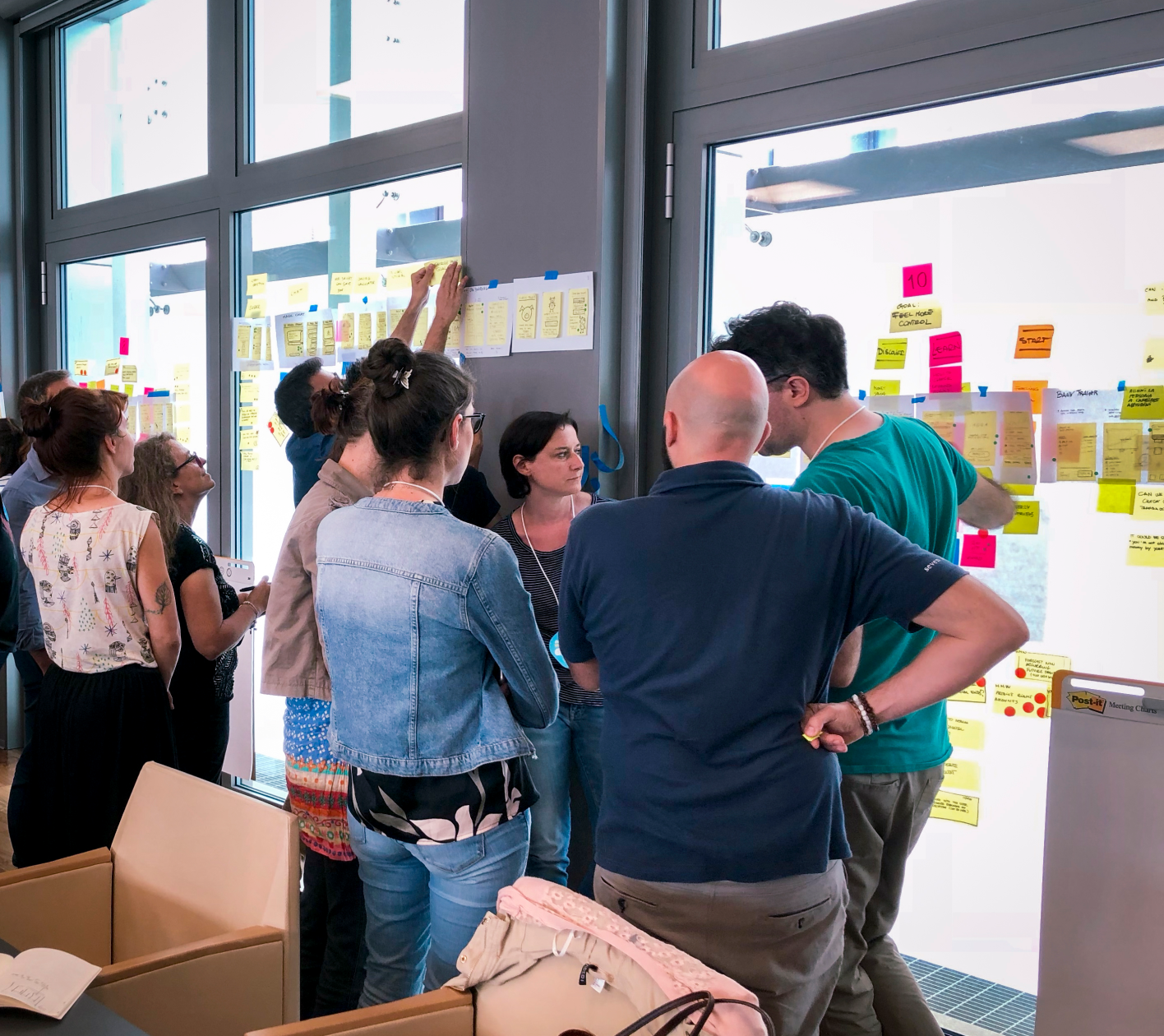 Three adults standing side by side indoors; woman on left smiling, man in center wearing colorful plaid shirt and glasses smiling, man on right with arms crossed and sunglasses hanging from his shirt.